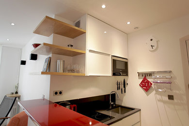 Idées déco pour une cuisine ouverte contemporaine en L de taille moyenne avec îlot, un évier intégré, un placard à porte affleurante, des portes de placard blanches, une crédence noire, un électroménager en acier inoxydable, parquet clair et un sol beige.