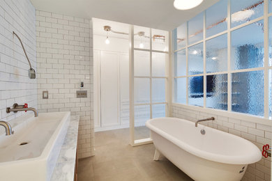Mid-sized industrial master bathroom in Vancouver with flat-panel cabinets, light wood cabinets, a claw-foot tub, a one-piece toilet, subway tile, white walls, limestone floors, a vessel sink and marble benchtops.