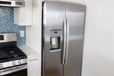 Kitchen - large modern galley vinyl floor, brown floor and coffered ceiling kitchen idea in Los Angeles with an undermount sink, shaker cabinets, white cabinets, quartzite countertops, blue backsplash, glass tile backsplash, stainless steel appliances, an island and white countertops