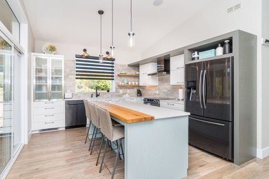 Example of a large transitional l-shaped light wood floor and brown floor kitchen design in Other with an undermount sink, flat-panel cabinets, white cabinets, quartz countertops, brown backsplash, subway tile backsplash, stainless steel appliances and an island