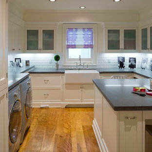 This is an example of a medium sized classic u-shaped separated utility room in Los Angeles with a belfast sink, glass-front cabinets, white cabinets, soapstone worktops, white walls, medium hardwood flooring and a side by side washer and dryer.