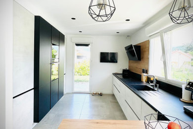 広いコンテンポラリースタイルのおしゃれなキッチン (一体型シンク、木材のキッチンパネル、パネルと同色の調理設備、セラミックタイルの床、グレーの床、黒いキッチンカウンター) の写真