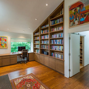 Inspiration for a medium sized modern home office and library in Cincinnati with a reading nook, white walls, medium hardwood flooring, a standard fireplace, a stone fireplace surround, a built-in desk and brown floors.