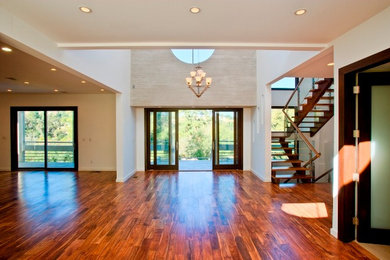 This is an example of a large modern foyer in Los Angeles with white walls, dark hardwood flooring, a sliding front door and a glass front door.