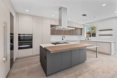 Example of a mid-sized minimalist u-shaped medium tone wood floor and brown floor open concept kitchen design in San Francisco with a single-bowl sink, flat-panel cabinets, light wood cabinets, quartz countertops, white backsplash, quartz backsplash, black appliances, an island and white countertops