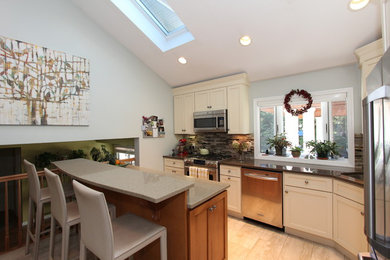 Example of a mid-sized transitional l-shaped beige floor kitchen design in New York with an undermount sink, shaker cabinets, beige cabinets, granite countertops, gray backsplash, stone tile backsplash, stainless steel appliances and an island