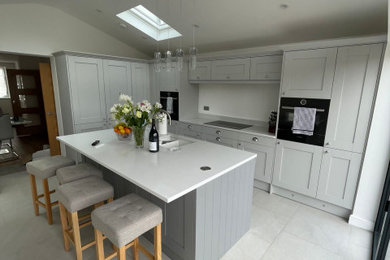 This is an example of a large contemporary grey and white l-shaped open plan kitchen in London with a built-in sink, shaker cabinets, grey cabinets, quartz worktops, multi-coloured splashback, stone slab splashback, integrated appliances, porcelain flooring, an island, grey floors, multicoloured worktops, a vaulted ceiling and feature lighting.