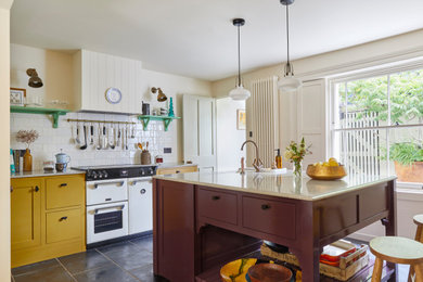 Large transitional limestone floor and black floor eat-in kitchen photo in London with a farmhouse sink, shaker cabinets, yellow cabinets, marble countertops, white backsplash, ceramic backsplash, white appliances, an island and brown countertops