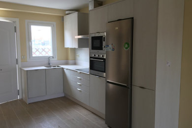 Diseño de cocina actual pequeña sin isla con armarios con paneles lisos, fregadero bajoencimera, puertas de armario de madera clara, encimera de cuarzo compacto, salpicadero blanco, salpicadero de vidrio, electrodomésticos de acero inoxidable y encimeras blancas