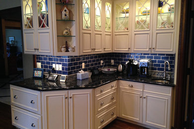 This is an example of a mid-sized arts and crafts l-shaped eat-in kitchen in Kansas City with glass-front cabinets, white cabinets, granite benchtops, blue splashback, subway tile splashback and medium hardwood floors.