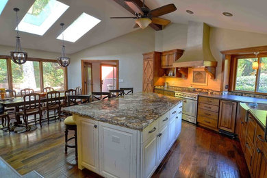 Large country l-shaped eat-in kitchen in San Francisco with a farmhouse sink, raised-panel cabinets, distressed cabinets, granite benchtops, multi-coloured splashback, stone tile splashback, stainless steel appliances, dark hardwood floors, with island, multi-coloured benchtop and brown floor.