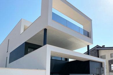 Ejemplo de fachada de casa blanca minimalista de tamaño medio de tres plantas con revestimiento de estuco y tejado plano