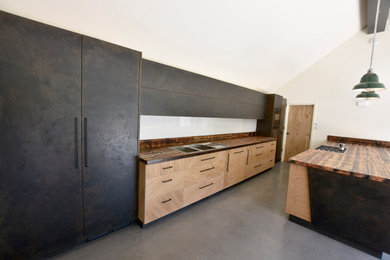 Large urban single-wall open plan kitchen in Oxfordshire with a double-bowl sink, flat-panel cabinets, light wood cabinets, wood worktops, white splashback, glass sheet splashback, black appliances, concrete flooring, an island, grey floors and multicoloured worktops.
