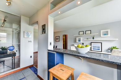 Small trendy l-shaped porcelain tile and gray floor open concept kitchen photo in DC Metro with a drop-in sink, flat-panel cabinets, blue cabinets, granite countertops, metallic backsplash and stainless steel appliances