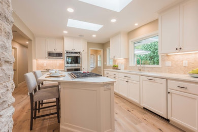 Eat-in kitchen - mid-sized l-shaped light wood floor and brown floor eat-in kitchen idea in Minneapolis with an undermount sink, shaker cabinets, white cabinets, beige backsplash, stainless steel appliances, an island, white countertops, quartz countertops and matchstick tile backsplash