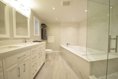 Photo of a large contemporary master bathroom in Toronto with recessed-panel cabinets, white cabinets, a drop-in tub, a corner shower, a two-piece toilet, gray tile, stone tile, grey walls, porcelain floors, an undermount sink, grey floor and a hinged shower door.