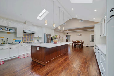 Eat-in kitchen - large transitional galley medium tone wood floor and brown floor eat-in kitchen idea in San Francisco with an undermount sink, recessed-panel cabinets, white cabinets, marble countertops, white backsplash, subway tile backsplash, stainless steel appliances, an island and white countertops