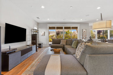 Ejemplo de sala de estar abierta minimalista grande sin chimenea con paredes grises, suelo de madera en tonos medios, televisor colgado en la pared y suelo marrón