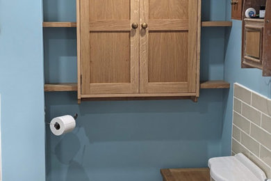 Photo of a small classic family bathroom in Oxfordshire with shaker cabinets, medium wood cabinets, a one-piece toilet, beige tiles, ceramic tiles, blue walls, laminate floors, brown floors, a single sink and a floating vanity unit.