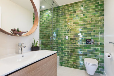 This is an example of a mid-sized contemporary 3/4 bathroom in San Francisco with flat-panel cabinets, beige cabinets, a wall-mount toilet, green tile, white walls, solid surface benchtops, white floor, a hinged shower door, a double shower, ceramic tile, ceramic floors, white benchtops and an integrated sink.