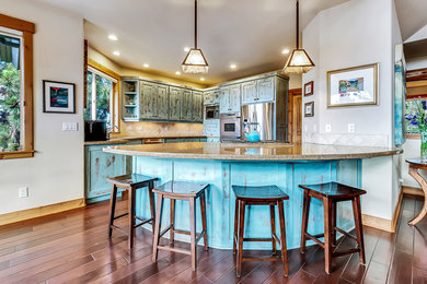 Example of a mid-sized mountain style l-shaped dark wood floor and brown floor enclosed kitchen design in Other with an undermount sink, recessed-panel cabinets, blue cabinets, granite countertops, beige backsplash, porcelain backsplash, stainless steel appliances and a peninsula