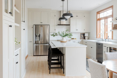 Example of a large transitional l-shaped light wood floor and brown floor eat-in kitchen design in Other with an undermount sink, shaker cabinets, white cabinets, quartz countertops, white backsplash, quartz backsplash, stainless steel appliances, an island and white countertops