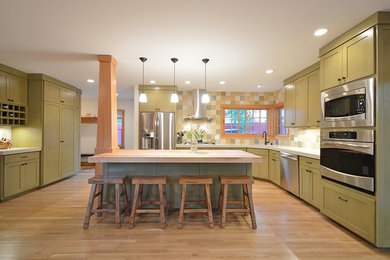Open concept kitchen - craftsman l-shaped light wood floor open concept kitchen idea in Other with an undermount sink, recessed-panel cabinets, green cabinets, multicolored backsplash, stainless steel appliances, an island and wood countertops