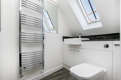 Photo of a small contemporary ensuite half tiled bathroom in Oxfordshire with flat-panel cabinets, white cabinets, an alcove shower, a one-piece toilet, grey tiles, white walls, vinyl flooring, a wall-mounted sink, laminate worktops, grey floors, a wall niche, a single sink, a built in vanity unit and a vaulted ceiling.