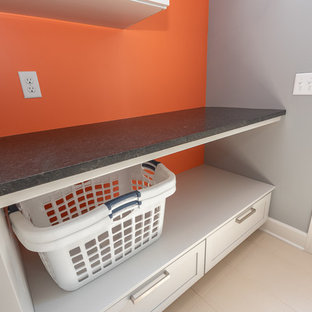 Foto de lavadero multiusos y lineal, tradicional, pequeño, con armarios con paneles empotrados, puertas de armario grises, encimera de granito, paredes grises, suelo de baldosas de cerámica, lavadora y secadora apiladas, suelo blanco y encimeras negras