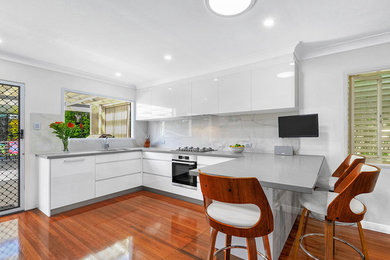 Inspiration for a mid-sized contemporary u-shaped open plan kitchen in Brisbane with a drop-in sink, flat-panel cabinets, white cabinets, quartz benchtops, multi-coloured splashback, porcelain splashback, stainless steel appliances, medium hardwood floors, a peninsula and orange floor.
