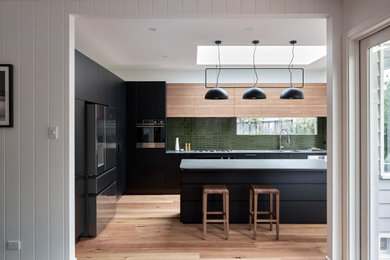 This is an example of a mid-sized contemporary l-shaped eat-in kitchen in Melbourne with an undermount sink, flat-panel cabinets, black cabinets, laminate benchtops, green splashback, porcelain splashback, stainless steel appliances, light hardwood floors, with island and grey benchtop.