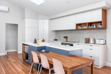 Photo of a contemporary l-shaped eat-in kitchen in Canberra - Queanbeyan with an undermount sink, flat-panel cabinets, white cabinets, grey splashback, cement tile splashback, panelled appliances, medium hardwood floors, with island, brown floor and white benchtop.