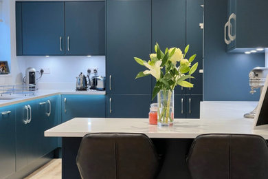 Large modern open plan kitchen in Kent with flat-panel cabinets, blue cabinets, quartz worktops, grey splashback, a breakfast bar and white worktops.
