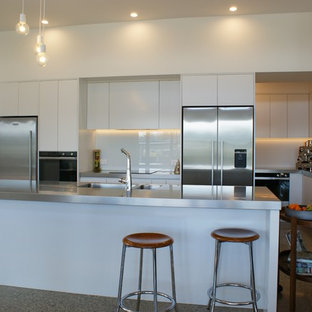 Large industrial kitchen pantry remodeling - Large urban galley concrete floor kitchen pantry photo in Dunedin with an integrated sink, flat-panel cabinets, white cabinets, stainless steel countertops, white backsplash, glass sheet backsplash, stainless steel appliances and an island