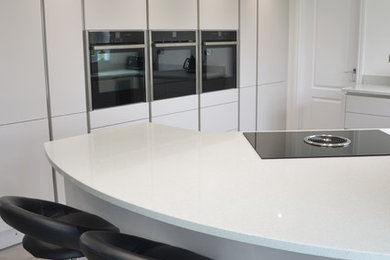 Inspiration for a medium sized modern l-shaped enclosed kitchen in Essex with a submerged sink, flat-panel cabinets, beige cabinets, quartz worktops, white splashback, black appliances, porcelain flooring, no island and grey floors.