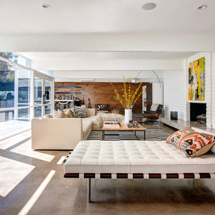 Imagen de salón abierto, contemporáneo, grande, sin televisor, con paredes blancas, suelo de cemento, chimenea tradicional, marco de chimenea de ladrillo y suelo marrón