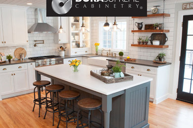 Inspiration for a mid-sized transitional u-shaped light wood floor eat-in kitchen remodel in Chicago with a farmhouse sink, recessed-panel cabinets, white cabinets, quartz countertops, multicolored backsplash, subway tile backsplash, stainless steel appliances and an island