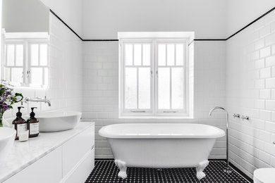 This is an example of a large traditional bathroom in Sydney with furniture-like cabinets, white cabinets, a freestanding tub, an open shower, a wall-mount toilet, white tile, subway tile, white walls, mosaic tile floors, a vessel sink, marble benchtops, black floor, an open shower and white benchtops.