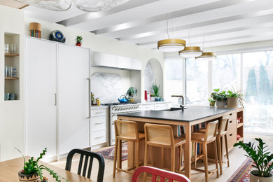 Inspiration for a large eclectic single-wall light wood floor and exposed beam eat-in kitchen remodel in Toronto with a farmhouse sink, shaker cabinets, white cabinets, granite countertops, multicolored backsplash, stone slab backsplash, paneled appliances, an island and black countertops