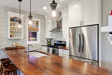 Inspiration for a mid-sized timeless galley medium tone wood floor open concept kitchen remodel in Chicago with an undermount sink, shaker cabinets, white cabinets, wood countertops, gray backsplash, wood backsplash, stainless steel appliances, an island and brown countertops