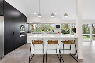 Photo of a large contemporary l-shaped kitchen pantry in Melbourne with a double-bowl sink, white cabinets, quartz benchtops, black appliances, terra-cotta floors and with island.