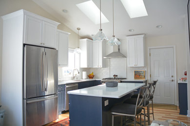 Klassisk inredning av ett mellanstort vit vitt kök, med en undermonterad diskho, skåp i shakerstil, blå skåp, bänkskiva i kvarts, vitt stänkskydd, stänkskydd i keramik, rostfria vitvaror, ljust trägolv, en köksö och brunt golv
