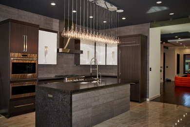Contemporary l-shaped kitchen in Chicago with an undermount sink, flat-panel cabinets, dark wood cabinets, grey splashback, panelled appliances, with island, brown floor and black benchtop.