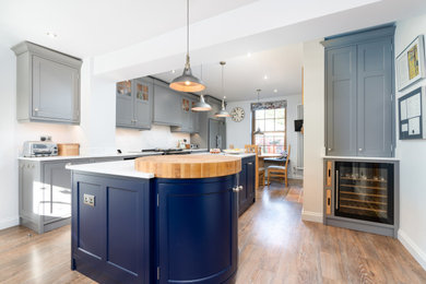 This is an example of a large traditional kitchen/diner in Other with an integrated sink, shaker cabinets, composite countertops, white splashback, black appliances, medium hardwood flooring, an island and white worktops.