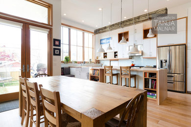 Example of a trendy l-shaped eat-in kitchen design in Calgary with a farmhouse sink, flat-panel cabinets, white cabinets, wood countertops, blue backsplash and stainless steel appliances