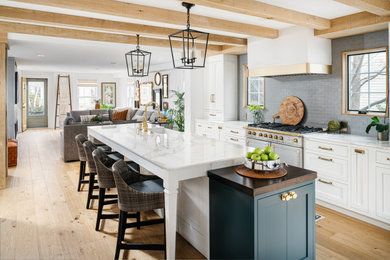 Example of a mid-sized farmhouse light wood floor, brown floor and exposed beam eat-in kitchen design in Philadelphia with an undermount sink, shaker cabinets, marble countertops, gray backsplash, subway tile backsplash, stainless steel appliances, an island and white countertops