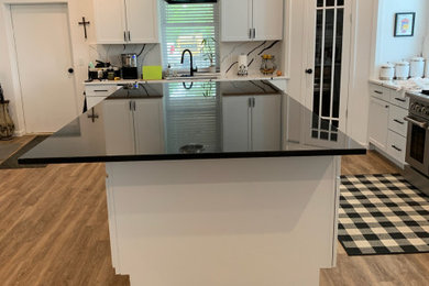 Eat-in kitchen - mid-sized cottage l-shaped eat-in kitchen idea in Other with an undermount sink, shaker cabinets, white cabinets, granite countertops, white backsplash, quartz backsplash, stainless steel appliances, an island and black countertops
