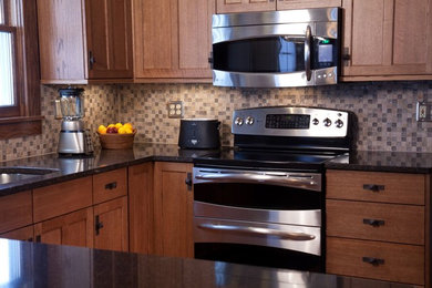 Open concept kitchen - mid-sized traditional u-shaped open concept kitchen idea in Milwaukee with an undermount sink, shaker cabinets, medium tone wood cabinets, solid surface countertops, multicolored backsplash, mosaic tile backsplash, stainless steel appliances and a peninsula