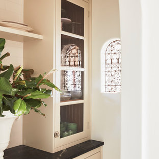 This is an example of an expansive mediterranean u-shaped kitchen pantry in Los Angeles with a farmhouse sink, raised-panel cabinets, white cabinets, limestone benchtops, white splashback, ceramic splashback, panelled appliances, dark hardwood floors, with island, brown floor and beige benchtop.