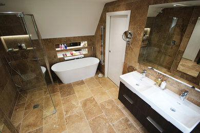 Photo of a large contemporary master bathroom in Surrey with flat-panel cabinets, brown cabinets, a freestanding tub, an open shower, a wall-mount toilet, brown tile, travertine, brown walls, travertine floors, an integrated sink and brown floor.